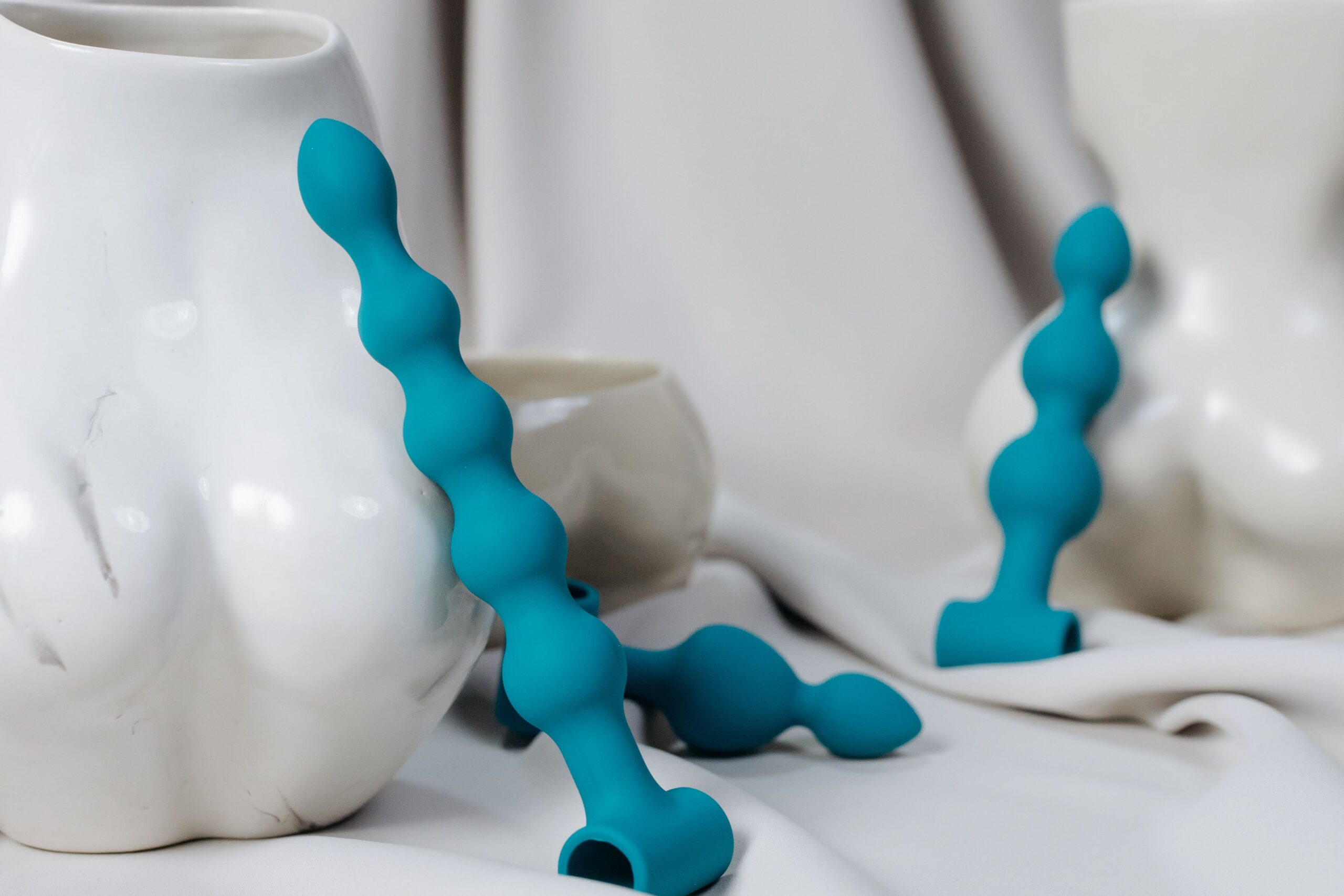 Artistic composition of blue silicone anal beads and vases. Soft lighting enhances the sensual aesthetic.